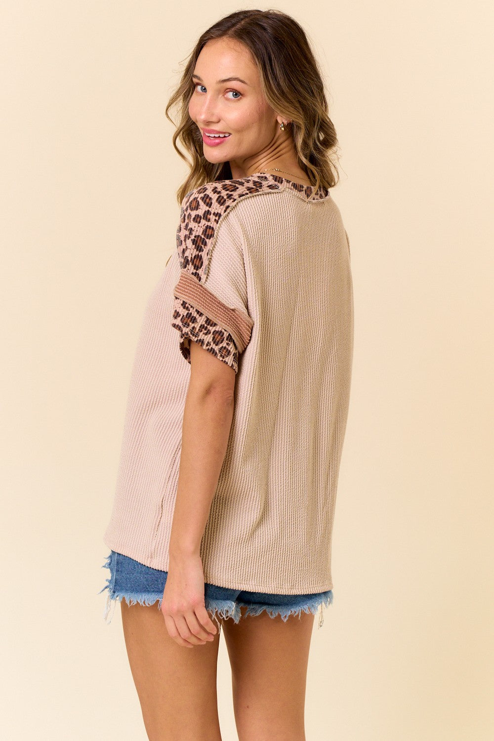 woman wearing a beige oversized top with leopard print sleeve detailing and styled with denim shorts