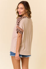 woman wearing a beige oversized top with leopard print sleeve detailing and styled with denim shorts