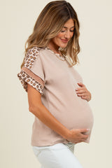 woman wearing a beige maternity top with leopard print sleeves and holding her baby bump