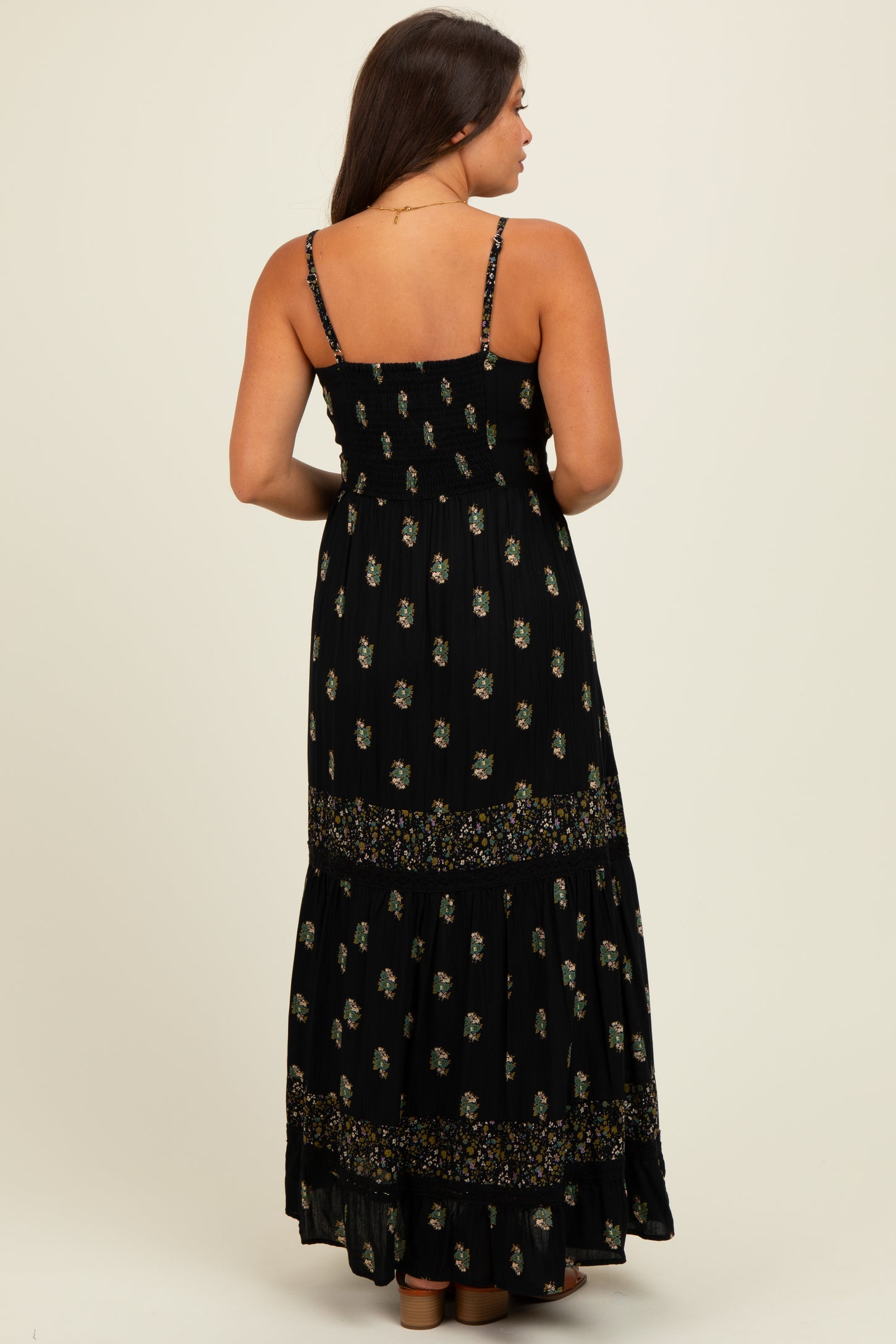 woman wearing a black floral print maternity maxi dress with adjustable straps and a tiered skirt, showing a baby bump