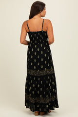 woman wearing a black floral print maternity maxi dress with adjustable straps and a tiered skirt, showing a baby bump