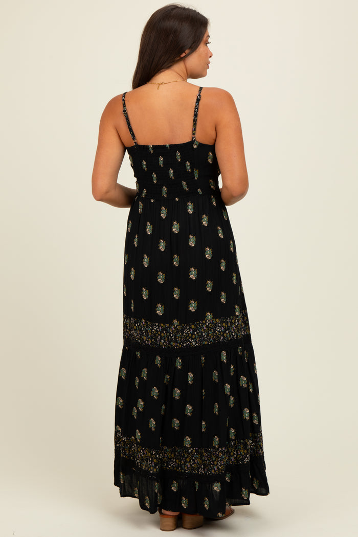 woman wearing a black floral print maternity maxi dress with adjustable straps and a tiered skirt, showing a baby bump