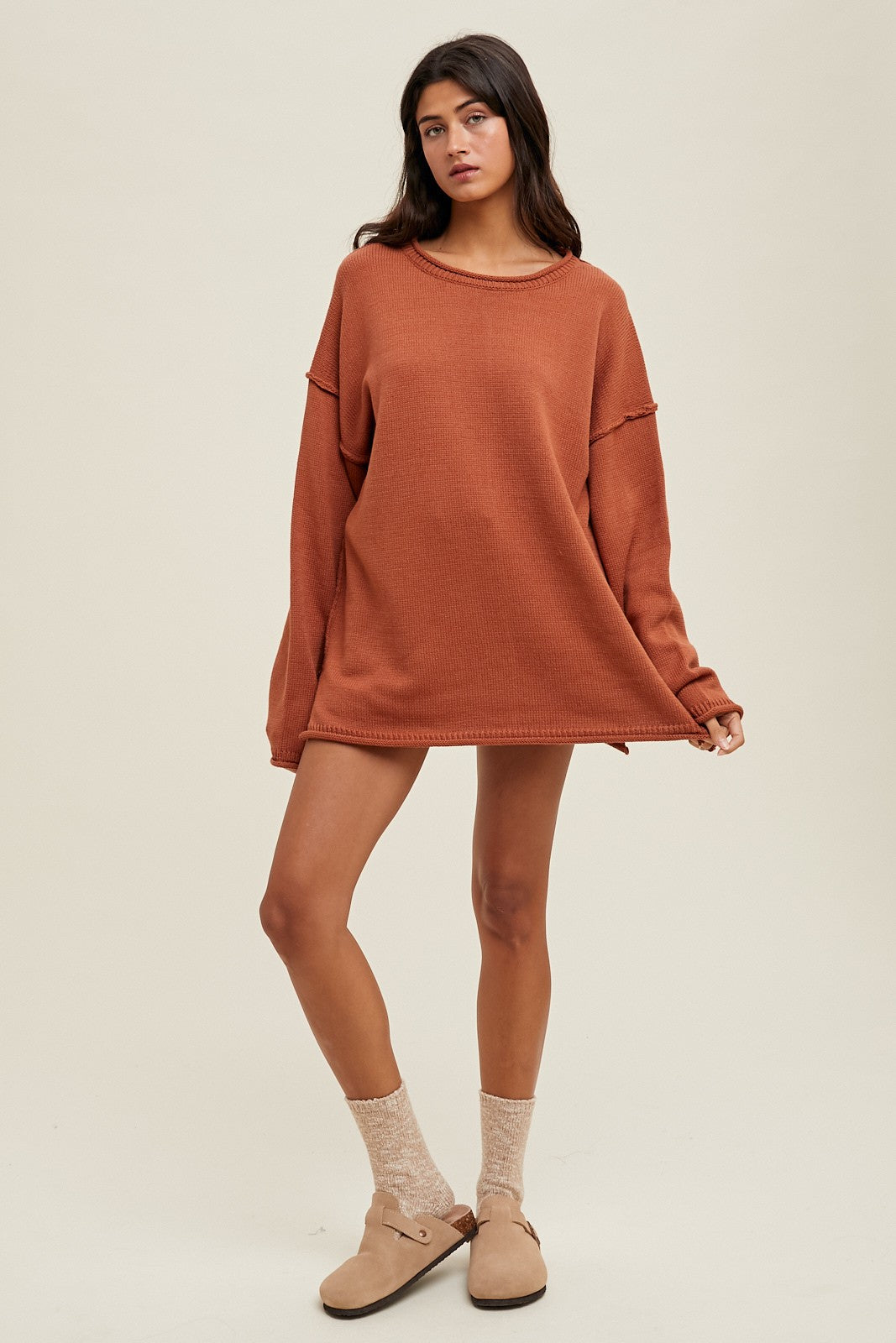 woman wearing a rust-colored oversized sweater dress with long sleeves and paired with cozy socks and slip-on shoes