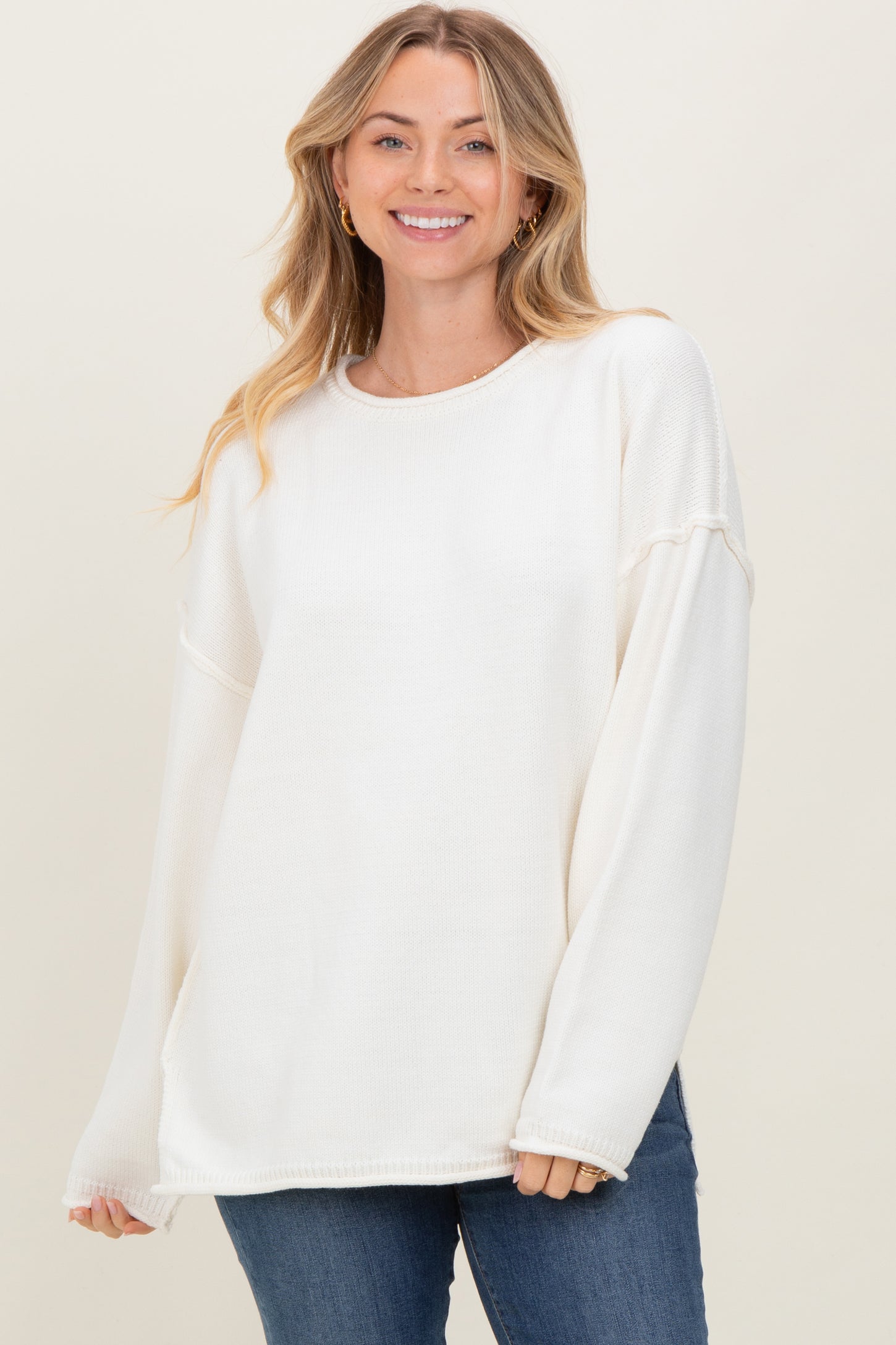 woman wearing a white oversized sweater with long sleeves and a relaxed fit, smiling at the camera