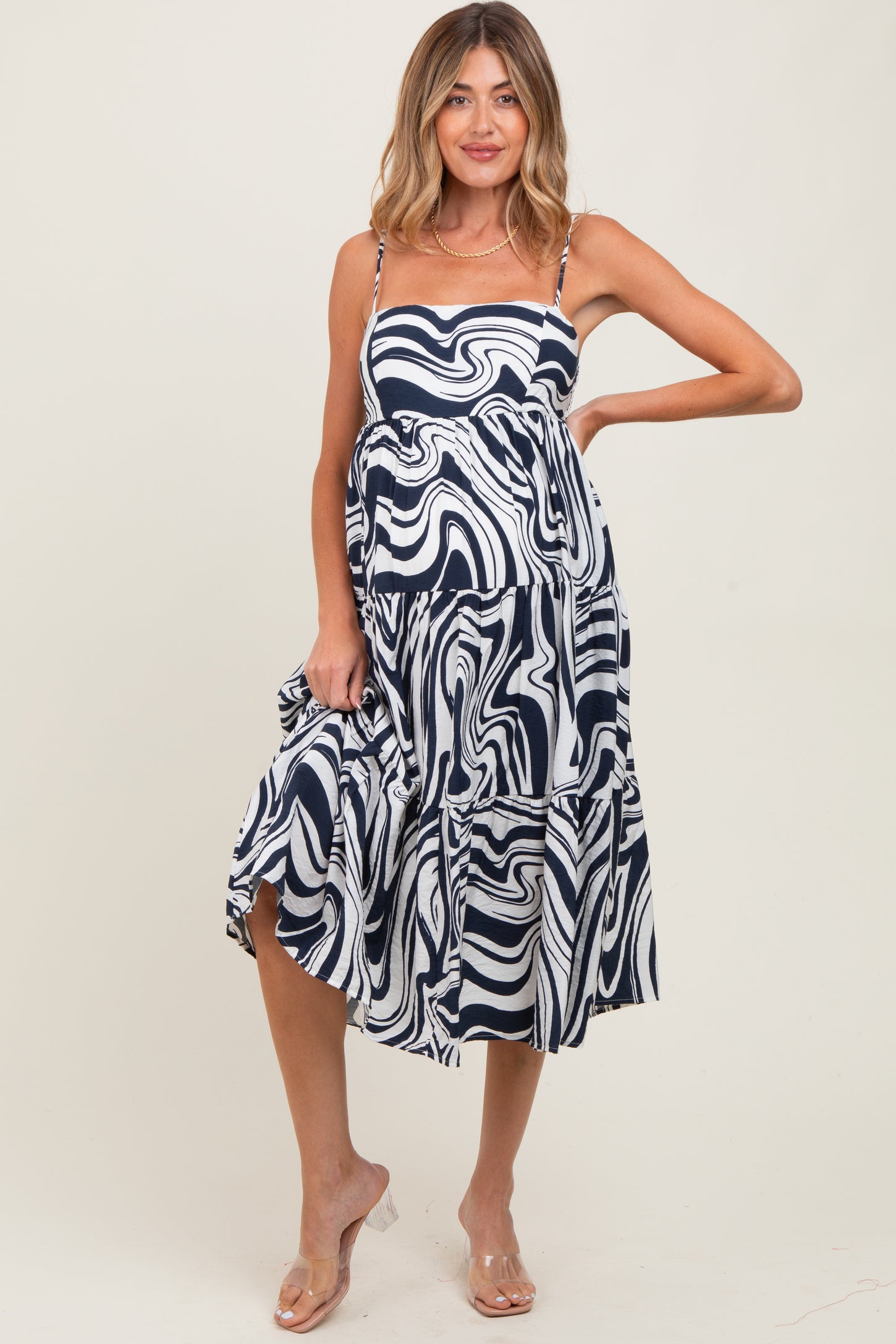 woman wearing a navy and white swirl pattern maternity dress with a tiered skirt and spaghetti straps, showing her baby bump