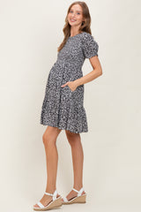 woman wearing a black and white floral maternity dress with puff sleeves and pockets, showing her baby bump