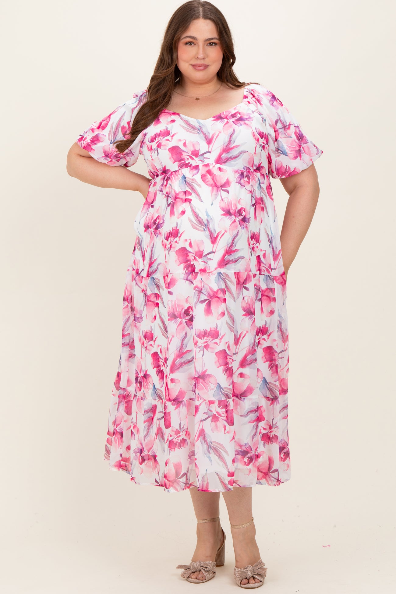 woman wearing a pink floral maternity plus dress with flutter sleeves and a flowing silhouette, showcasing her baby bump