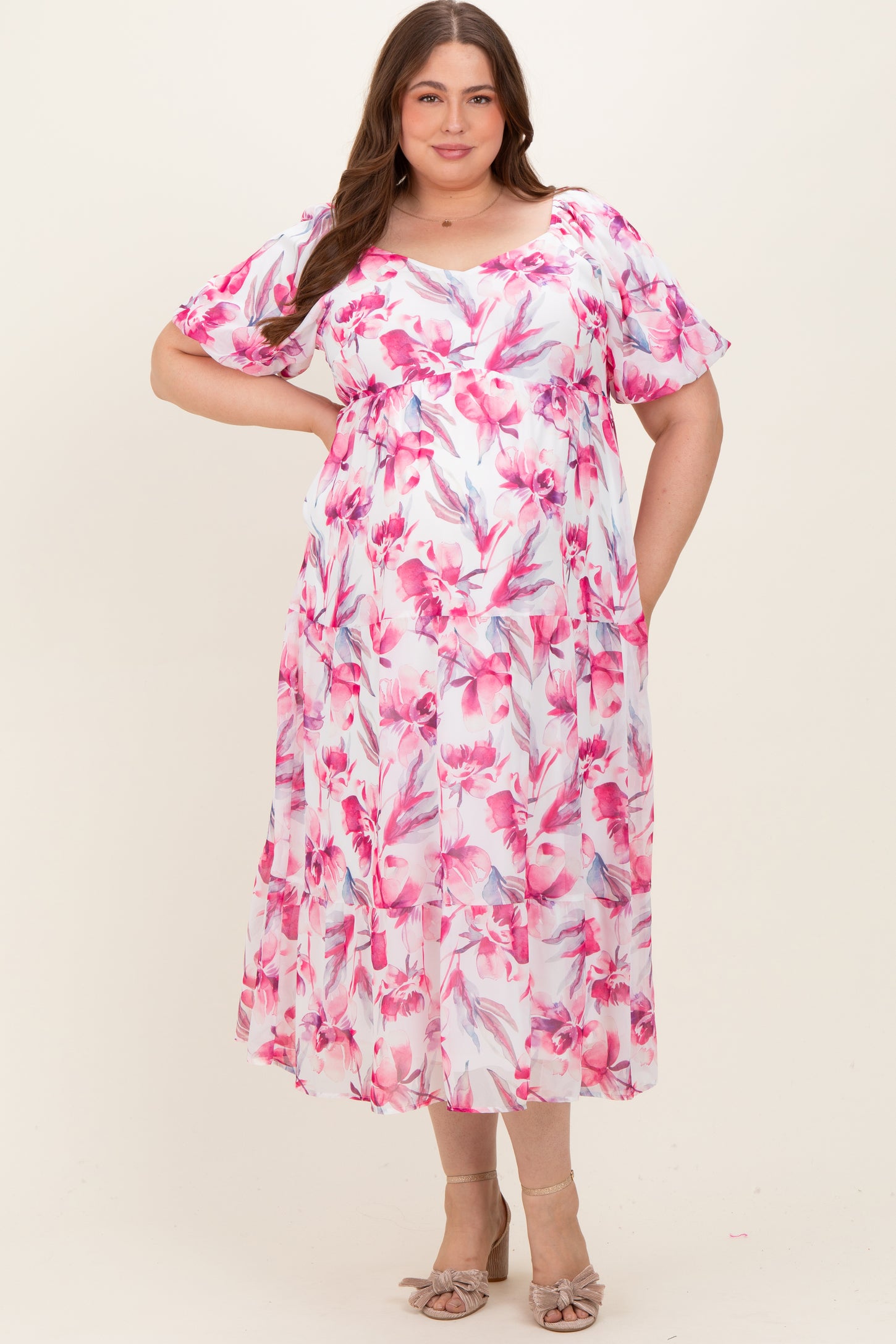 woman wearing a pink floral maternity plus dress with flutter sleeves and a flowing silhouette, showcasing her baby bump
