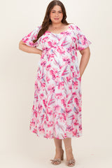 woman wearing a pink floral maternity plus dress with flutter sleeves and a flowing silhouette, showcasing her baby bump