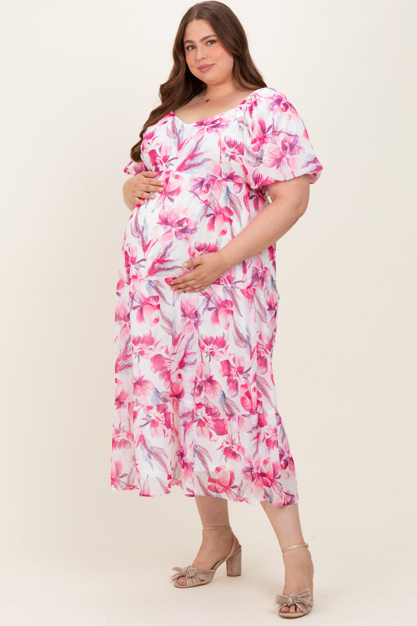 woman wearing a pink floral maternity dress with tiered design, holding her baby bump