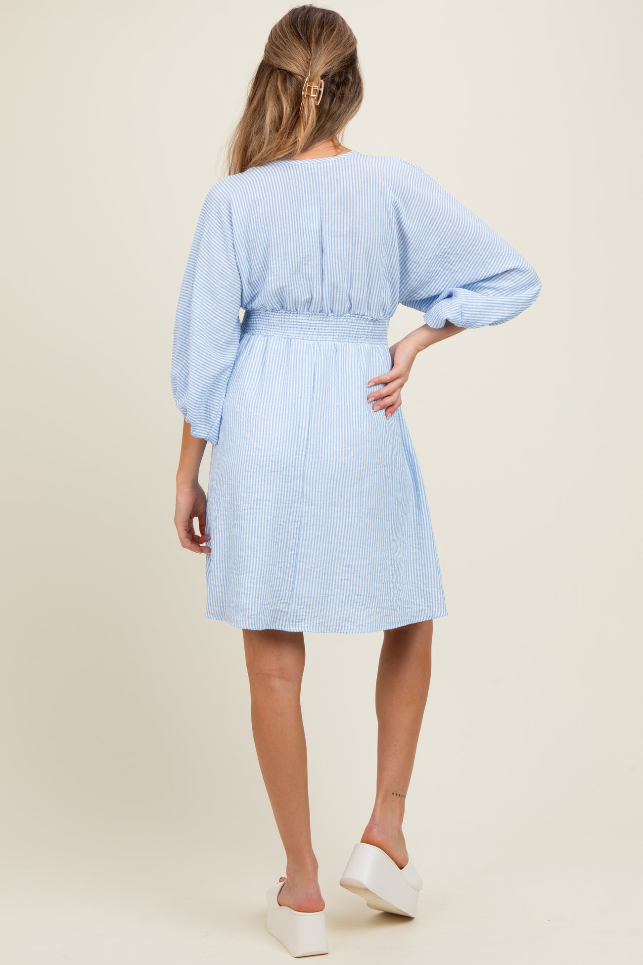 woman wearing a light blue striped maternity dress with a belted waist and balloon sleeves, shown from the back