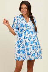woman wearing a white maternity dress with blue floral print and short sleeves, holding one hand up in a playful pose