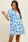 woman wearing a white maternity dress with blue floral print and short sleeves, holding one hand up in a playful pose