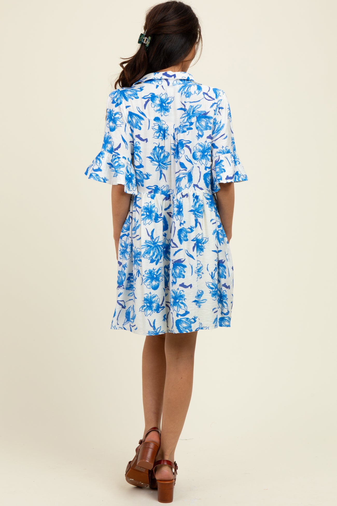 woman wearing a blue and white floral short sleeve dress with a loose fit and flared sleeves, standing with her back to the camera