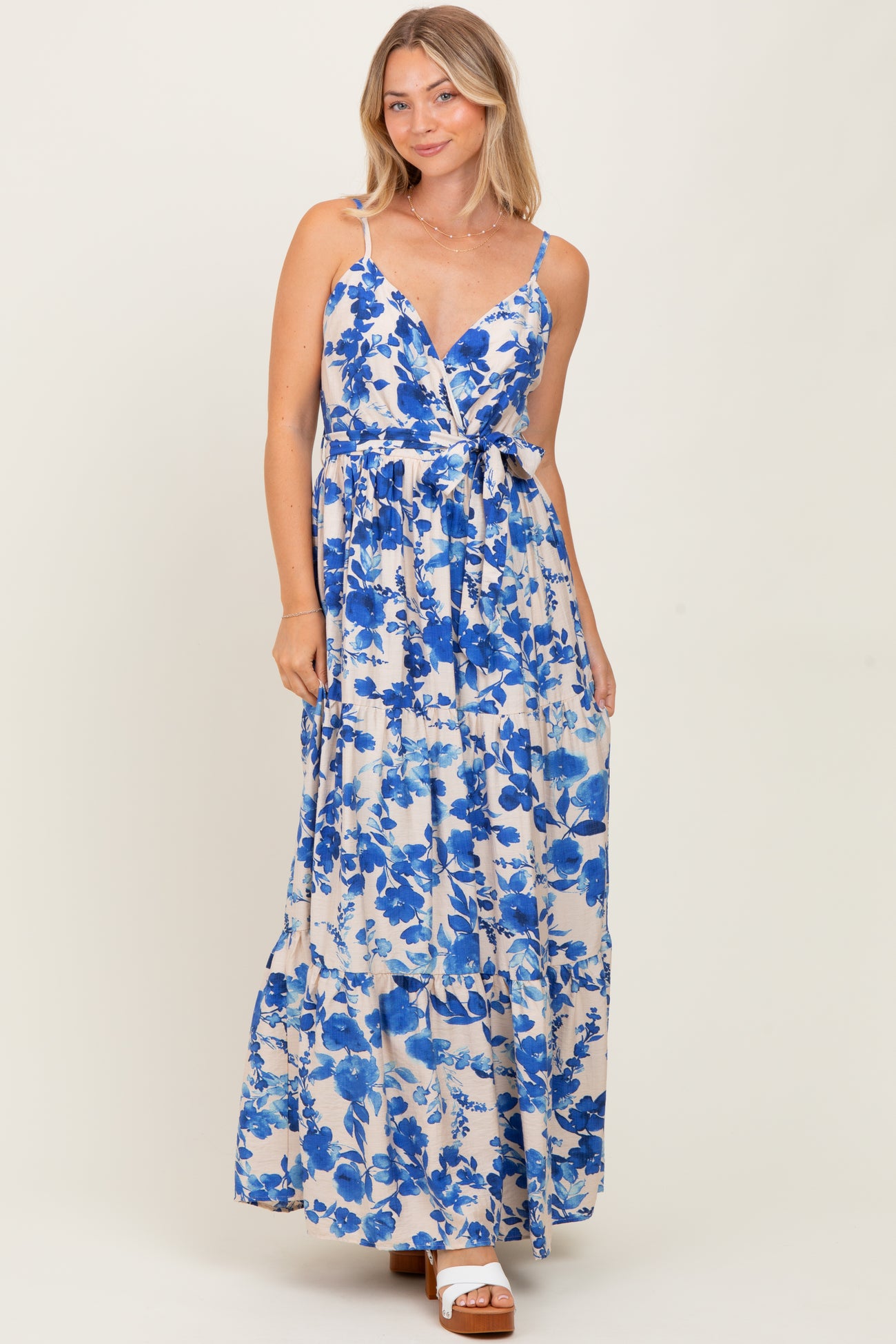 woman wearing a floral print maxi dress with blue and white hues, featuring a tie waist and adjustable straps
