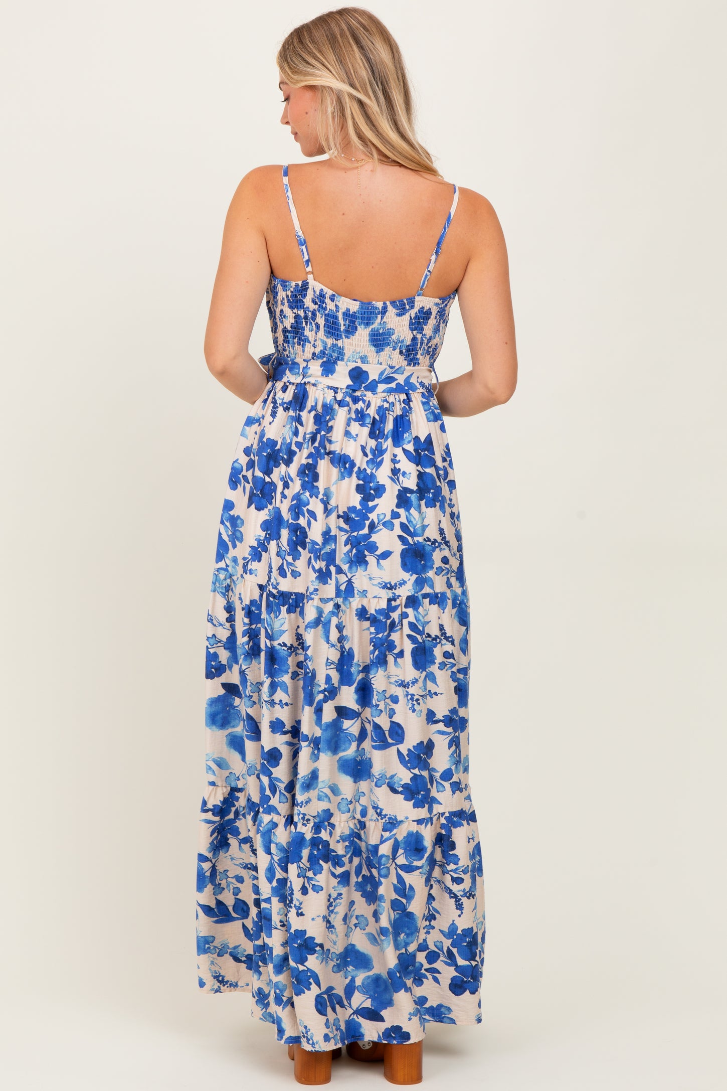 woman wearing a blue and white floral maxi dress with spaghetti straps, showcasing a smocked bodice and tiered skirt.