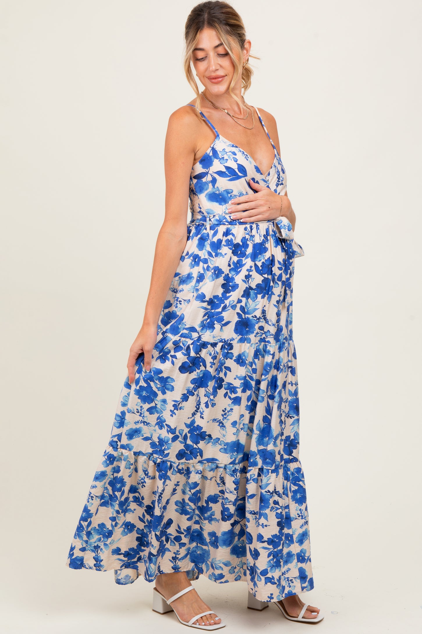 woman wearing a floral blue maternity maxi dress with spaghetti straps and tiered hem, highlighting her baby bump