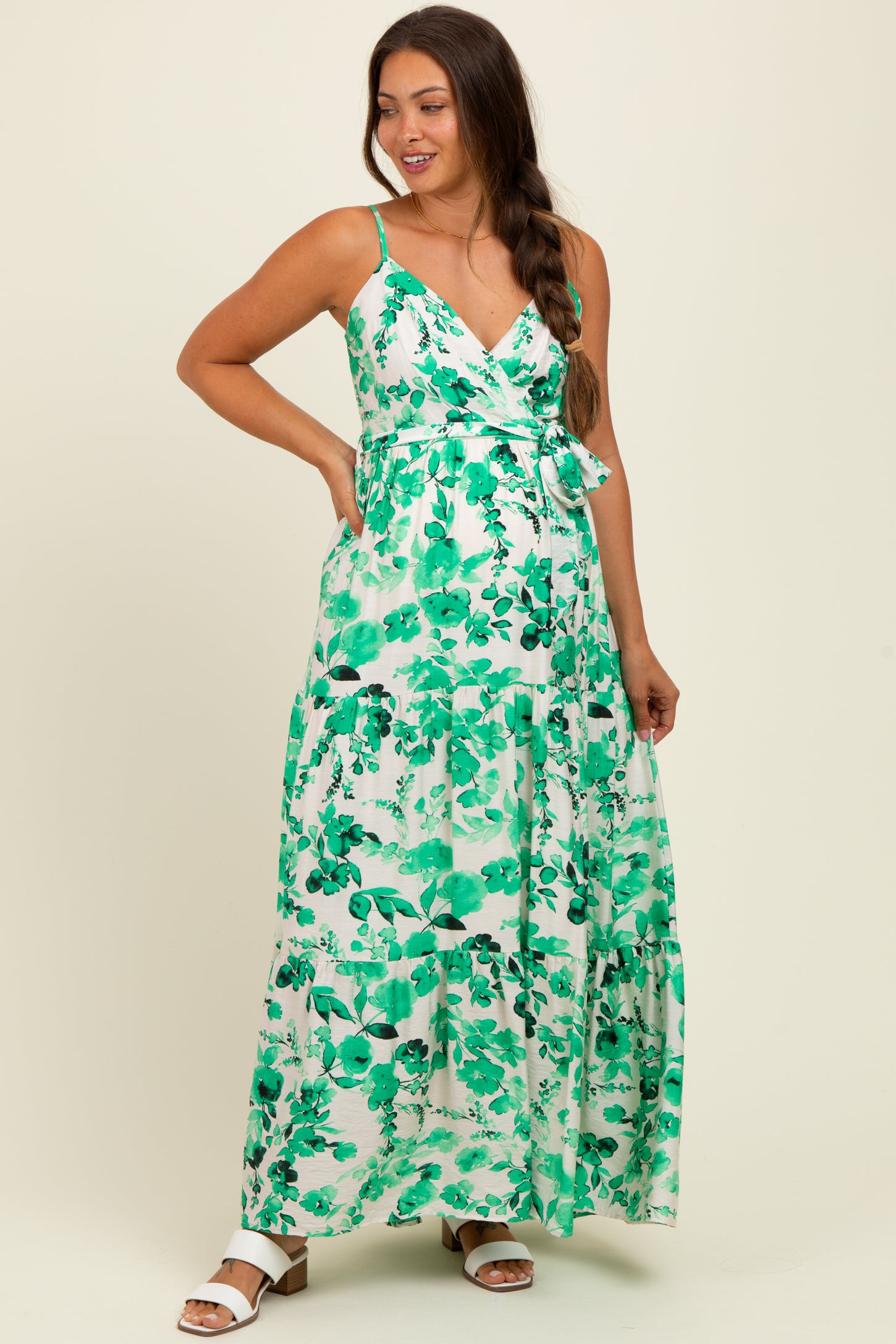 woman wearing a green floral maxi maternity dress with a tie waist and spaghetti straps, showing her baby bump