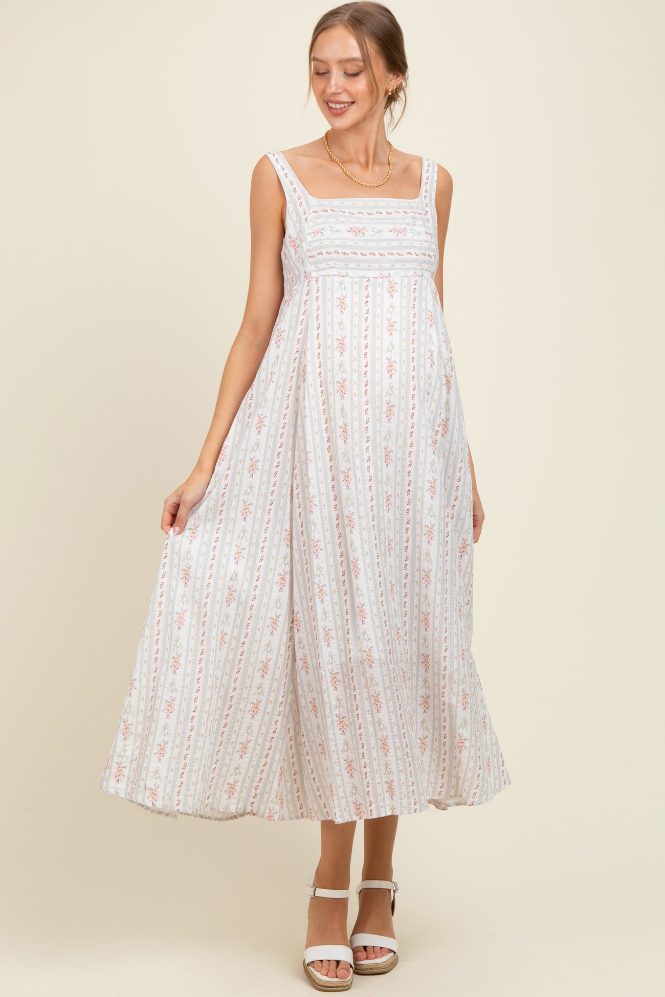 woman wearing a white floral print maternity maxi dress with a square neckline and a visible baby bump