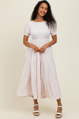 woman wearing a light pink tiered midi dress with short puff sleeves and a textured fabric, standing against a neutral background