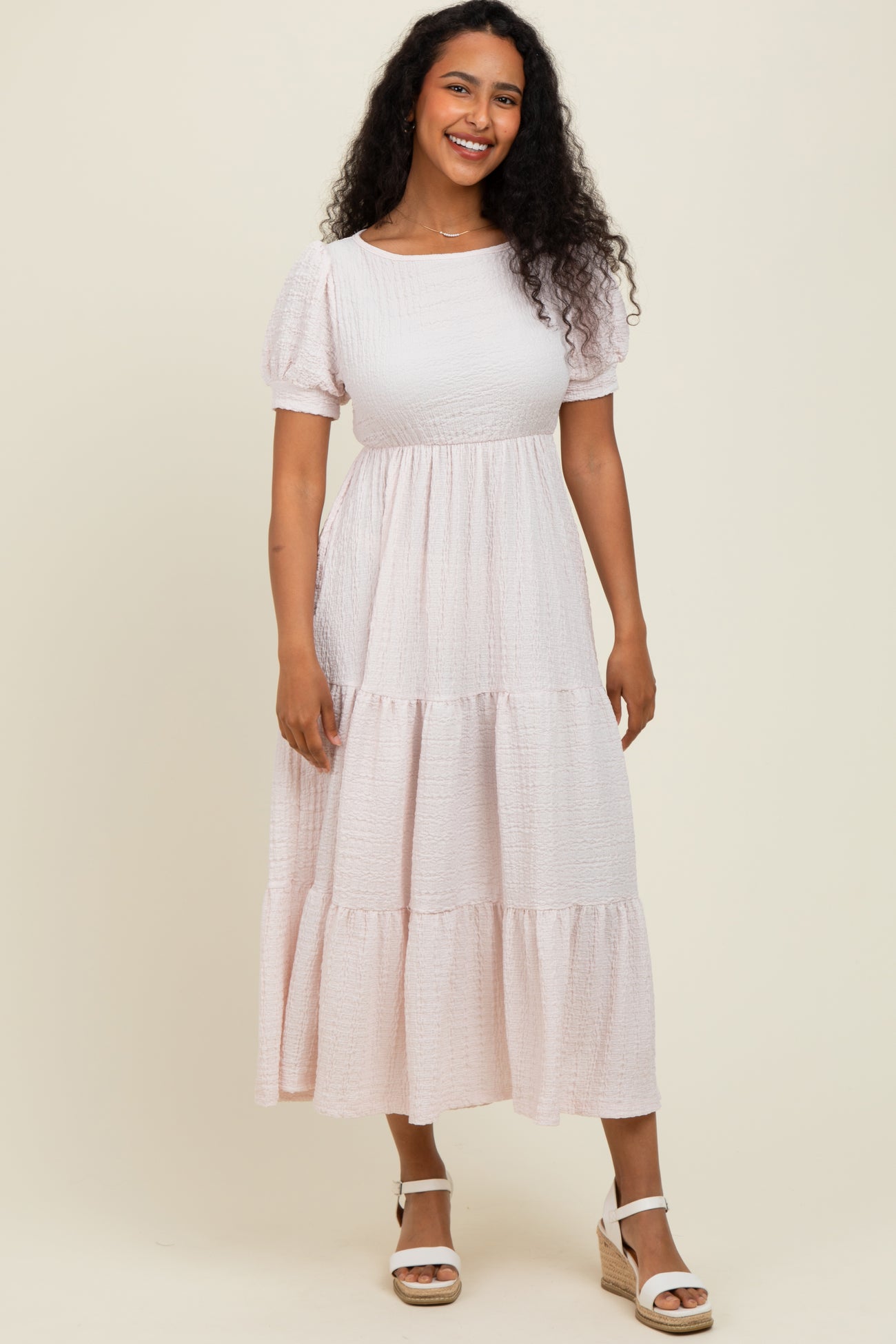 woman wearing a light pink puff sleeve midi dress with tiered layers and a relaxed fit