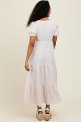 woman wearing a light pink tiered midi dress with puff sleeves, showing the back view and textured fabric