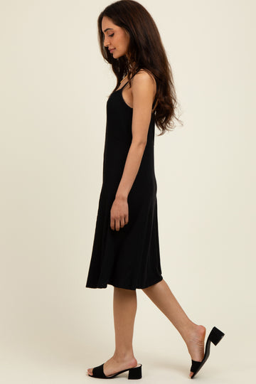 woman wearing a black ribbed slip dress with adjustable straps and a flared hem, standing sideways