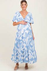 woman wearing a blue and white patterned maternity maxi dress and holding her baby bump