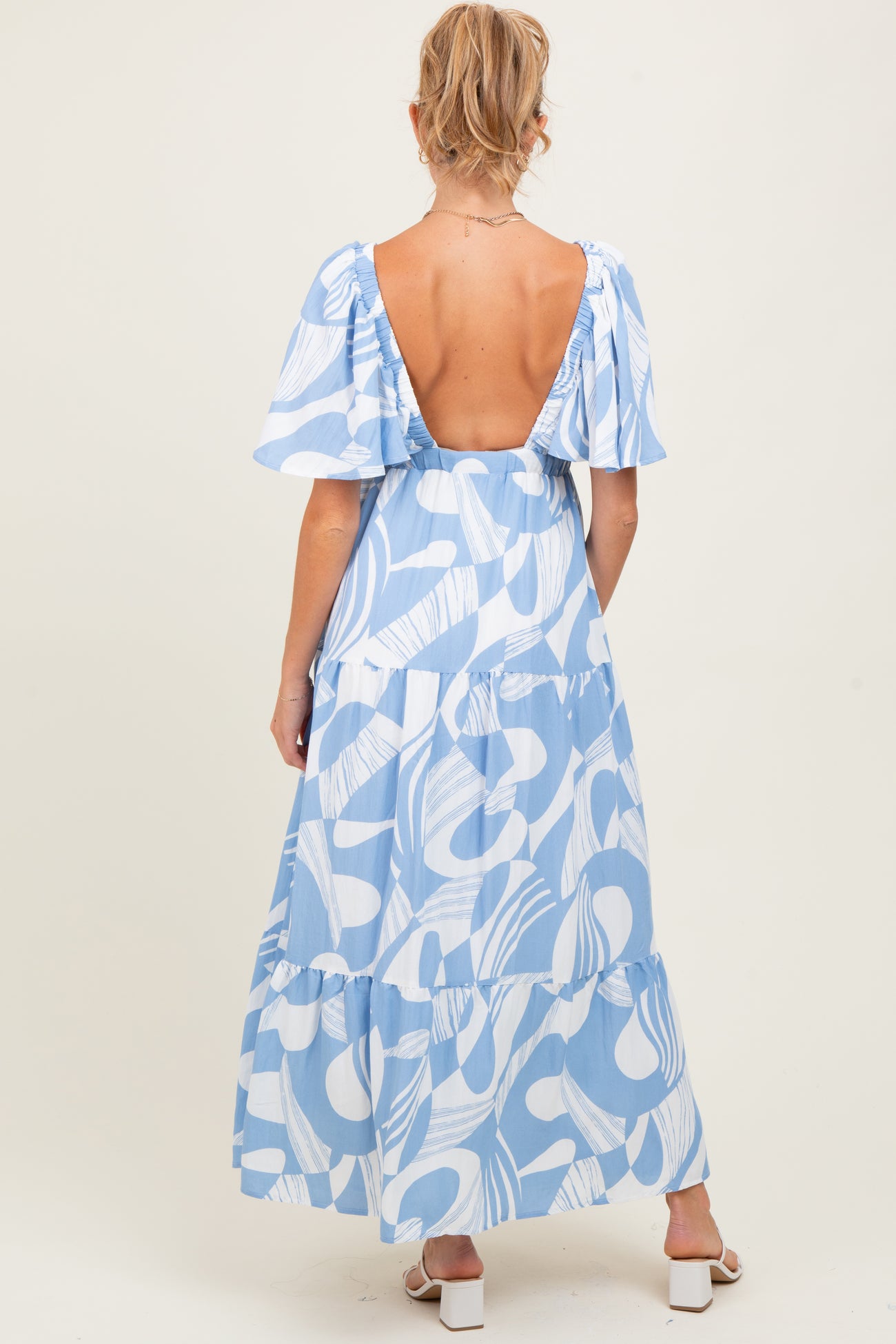 woman wearing a blue and white patterned maternity maxi dress with a low back and flutter sleeves