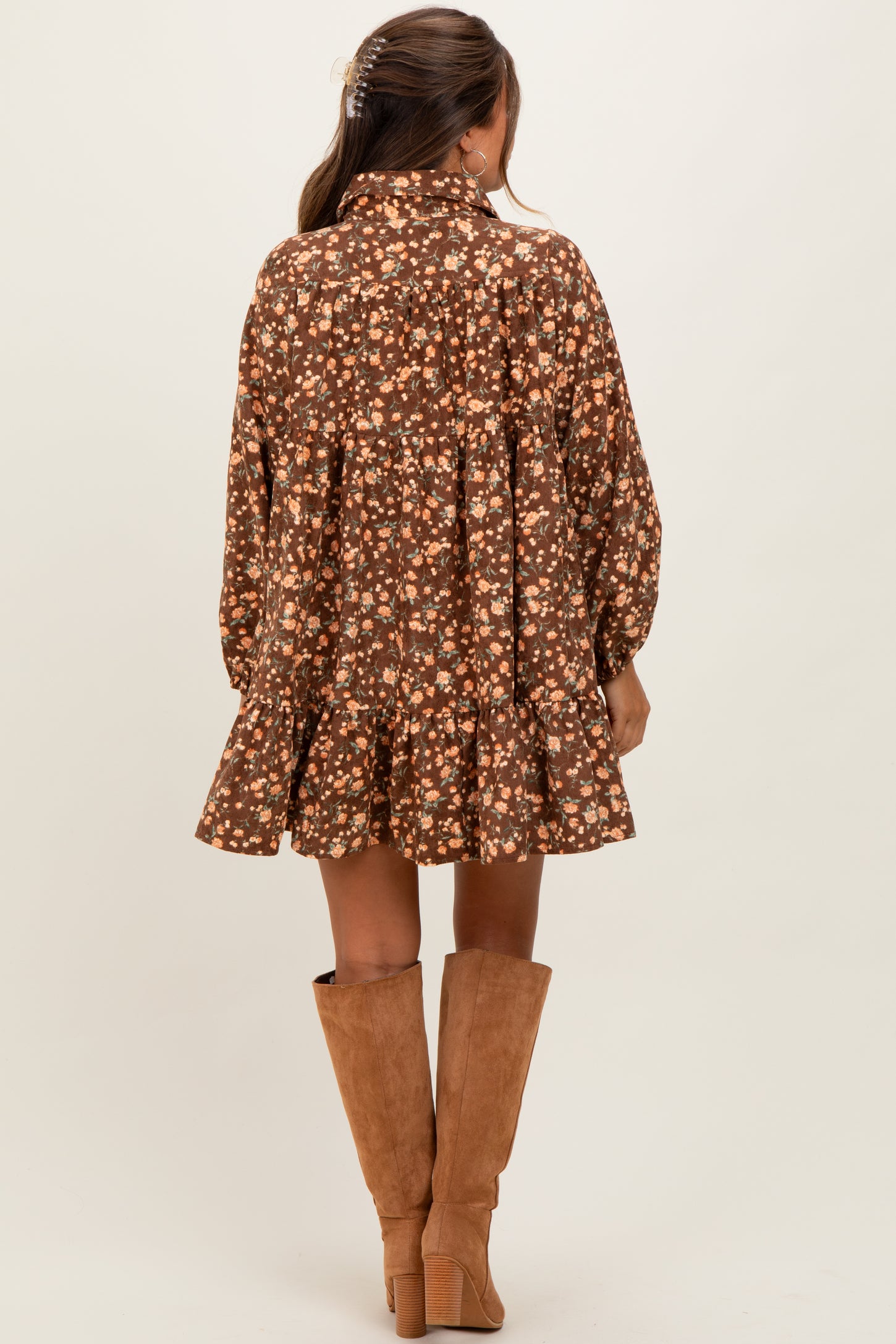 woman wearing a brown floral maternity dress with a tiered skirt and long sleeves, styled with knee-high tan boots
