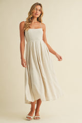woman wearing a light beige spaghetti strap maxi dress with pleats and a flowy silhouette