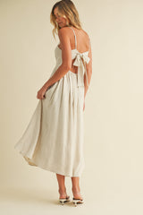 woman wearing a beige backless midi dress with a bow detail and a flowy skirt
