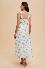woman wearing a white floral midi dress with blue accents, showcasing a smocked back and wide straps
