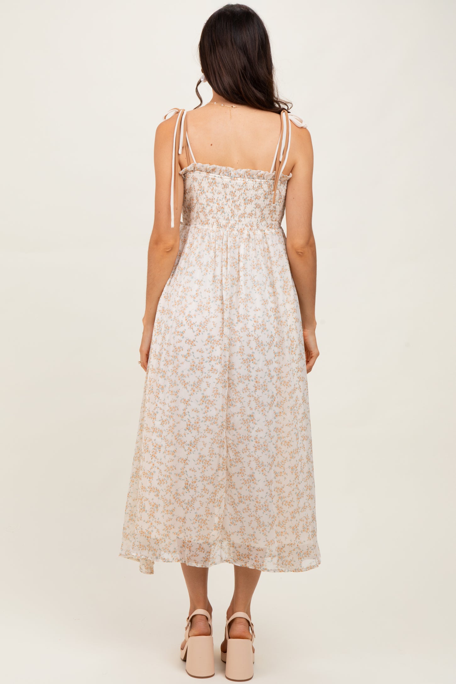 woman wearing a light floral midi dress with smocked bodice and tie shoulder straps, standing with back to the camera