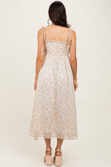 woman wearing a light floral midi dress with smocked bodice and tie shoulder straps, standing with back to the camera