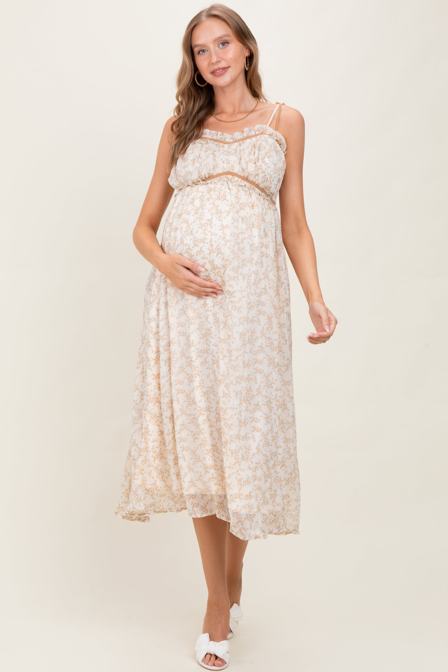 woman wearing a cream floral maternity maxi dress and holding her baby bump