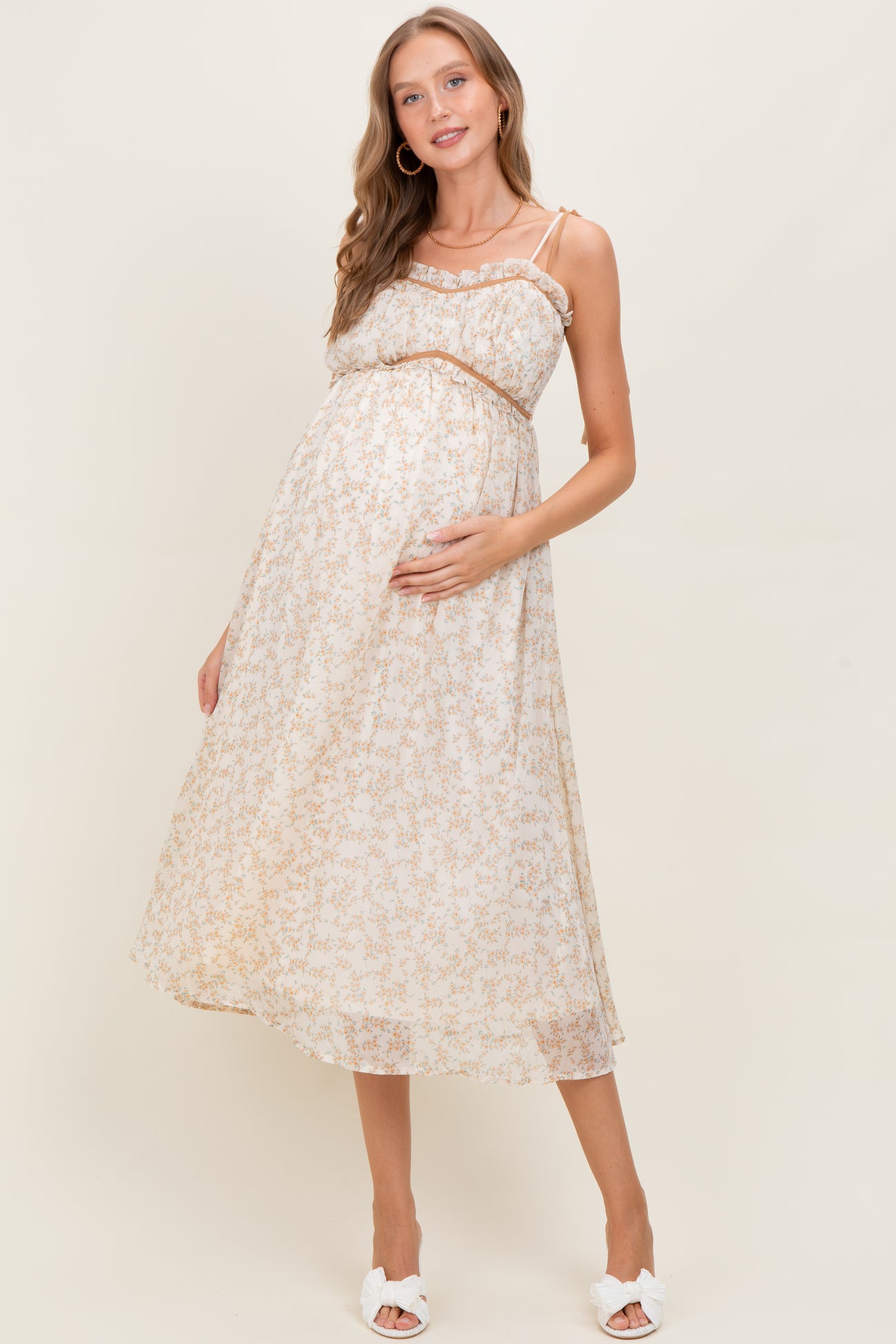 woman wearing a floral print maternity dress with a fitted bodice and flowing skirt, cradling her baby bump