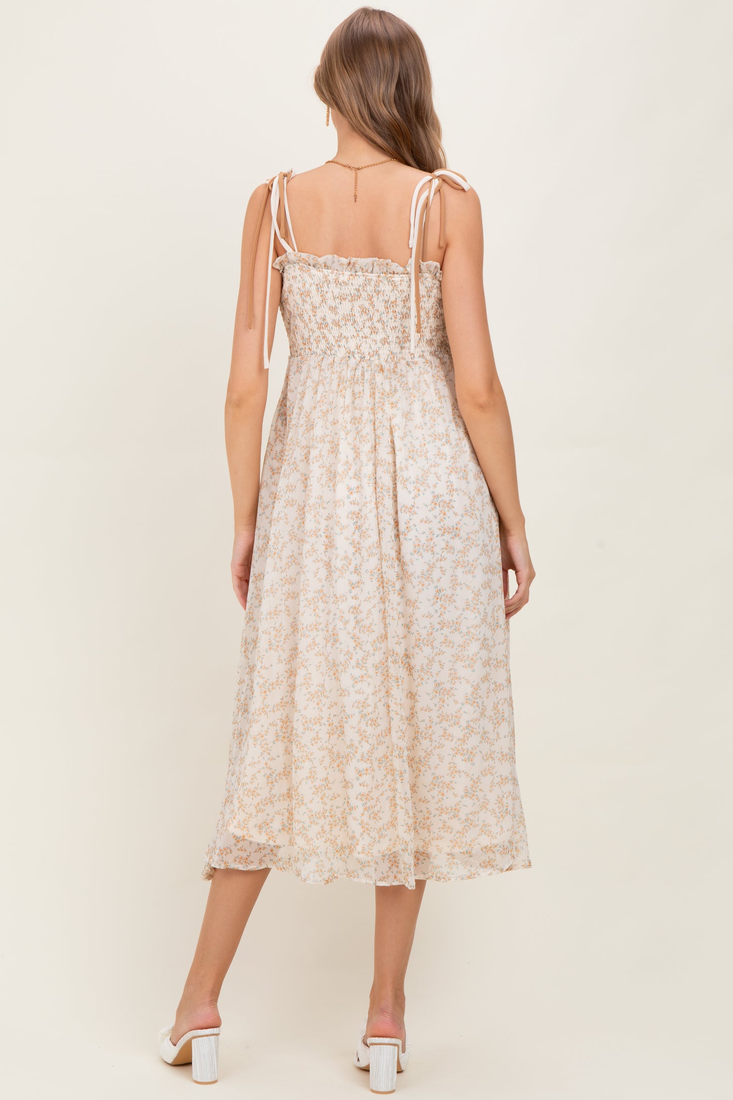 woman wearing a light floral print maternity dress with adjustable tie straps and a smocked back