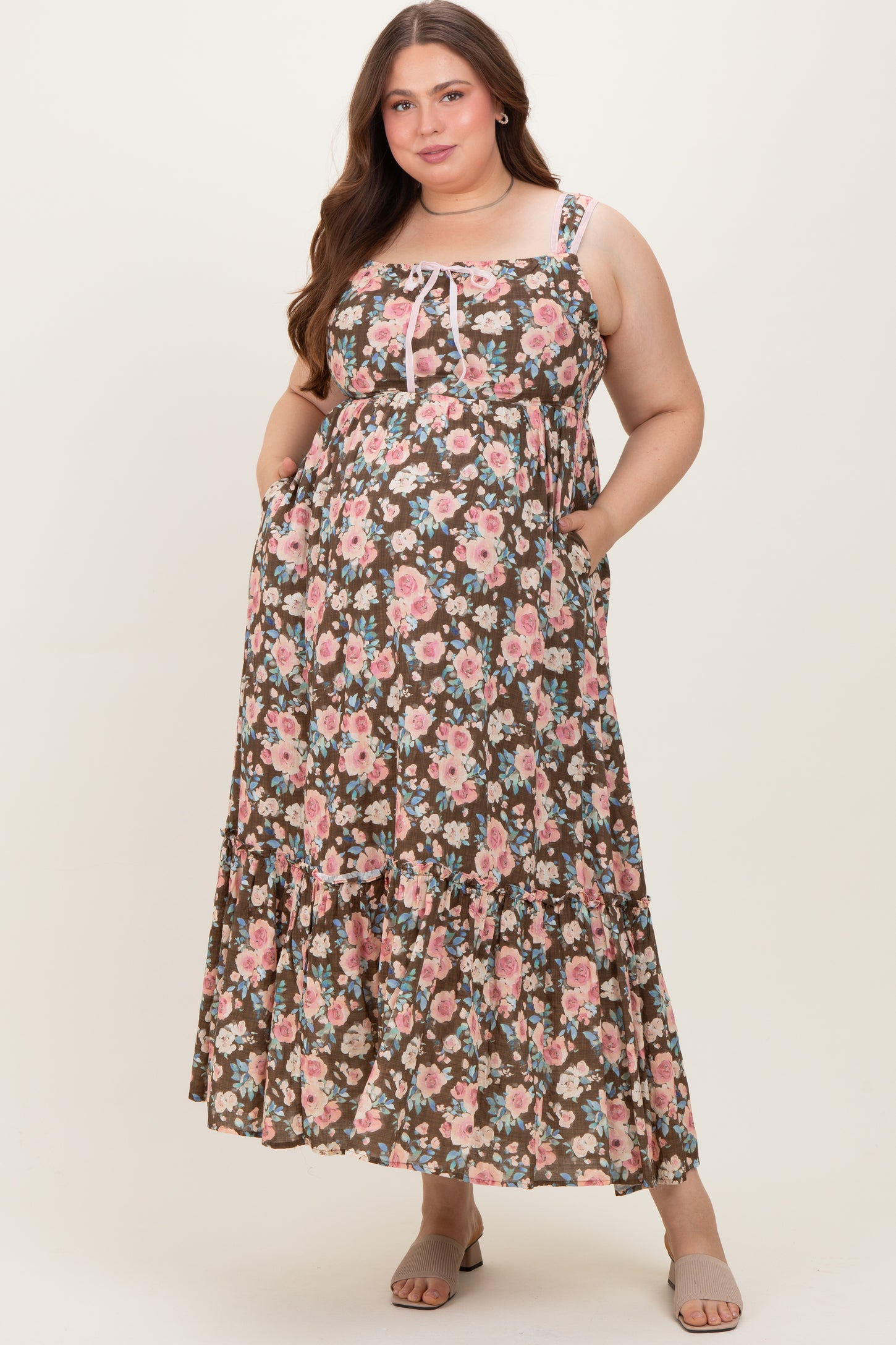 woman wearing a floral brown maternity plus maxi dress with pockets and adjustable straps, showcasing her baby bump