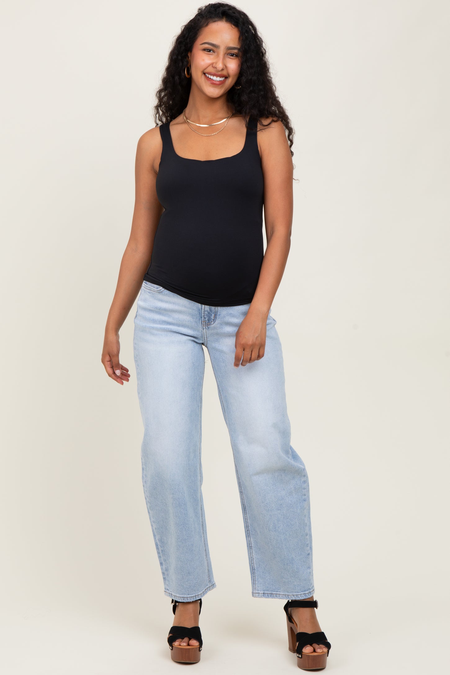 woman wearing a black maternity tank top and light blue wide-leg jeans, showing her baby bump