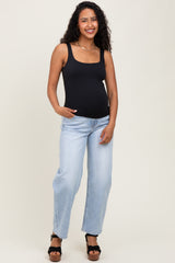 woman wearing a black maternity tank top and light blue distressed jeans, showing her baby bump while smiling