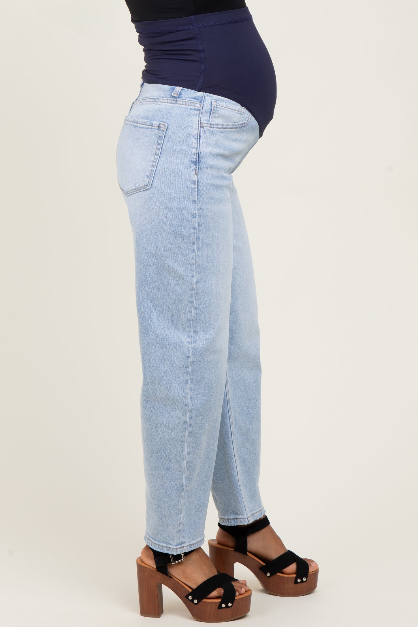 woman wearing light wash maternity jeans with a visible baby bump and black platform sandals
