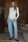 woman wearing a white long sleeve maternity top and light blue maternity jeans, showing her baby bump