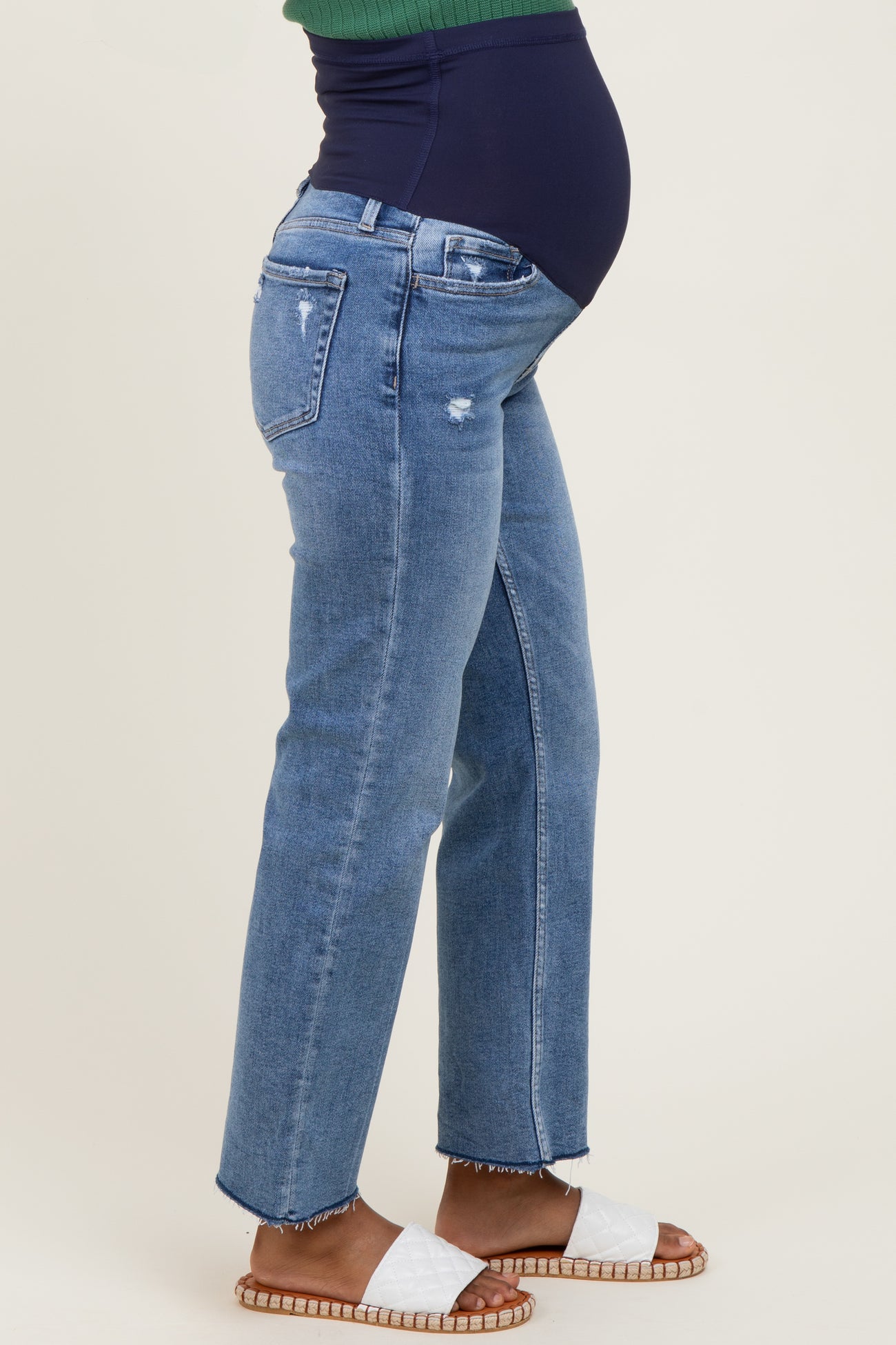 woman wearing distressed light blue maternity jeans with a visible baby bump and flat sandals