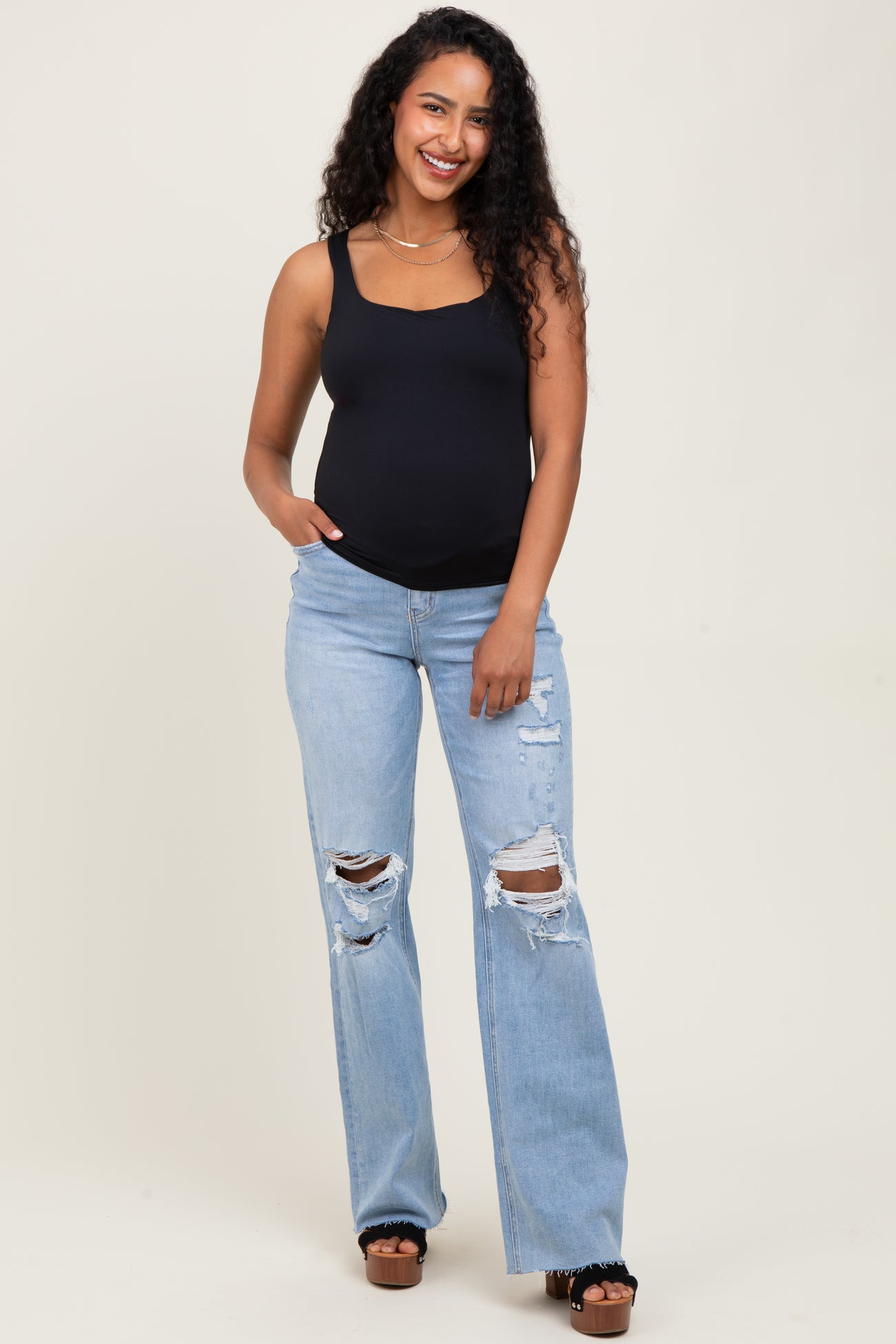 woman wearing a black maternity tank top and distressed light blue maternity jeans with a visible baby bump