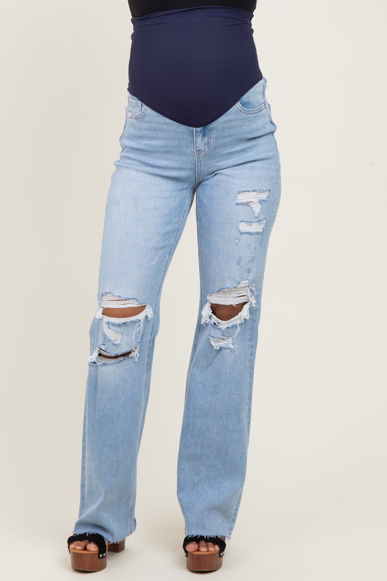 woman wearing light blue distressed maternity jeans with rips and a fitted navy top, showcasing her baby bump