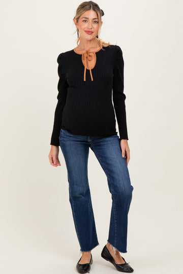 woman wearing a black ribbed maternity top with a tied neckline and blue flared jeans, showing her baby bump