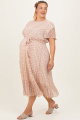 woman wearing a light pink floral maternity dress with a tie waist and short sleeves, showcasing her baby bump