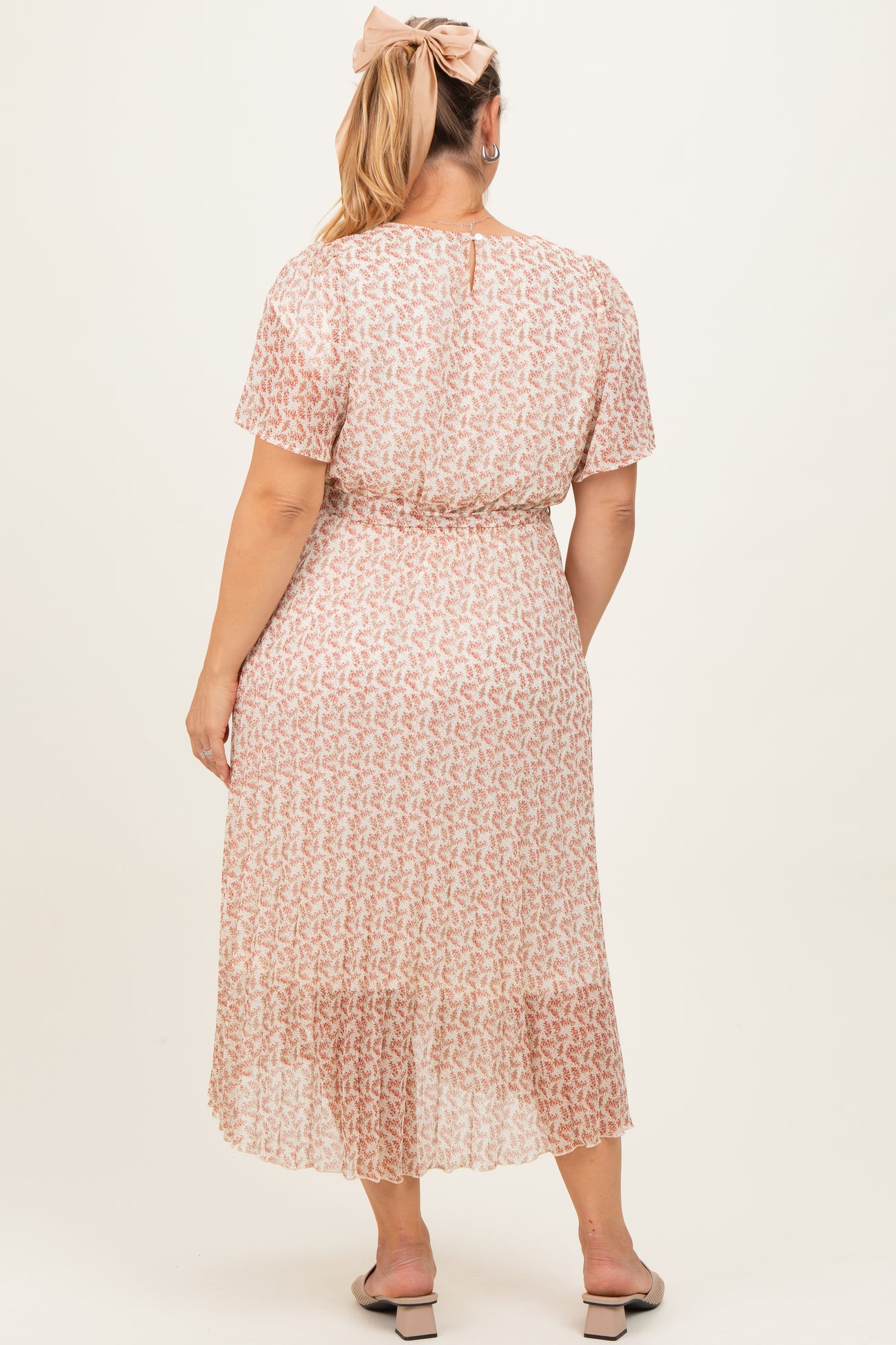woman wearing a light pink floral maternity plus dress with a waist tie and flutter sleeves, viewed from the back