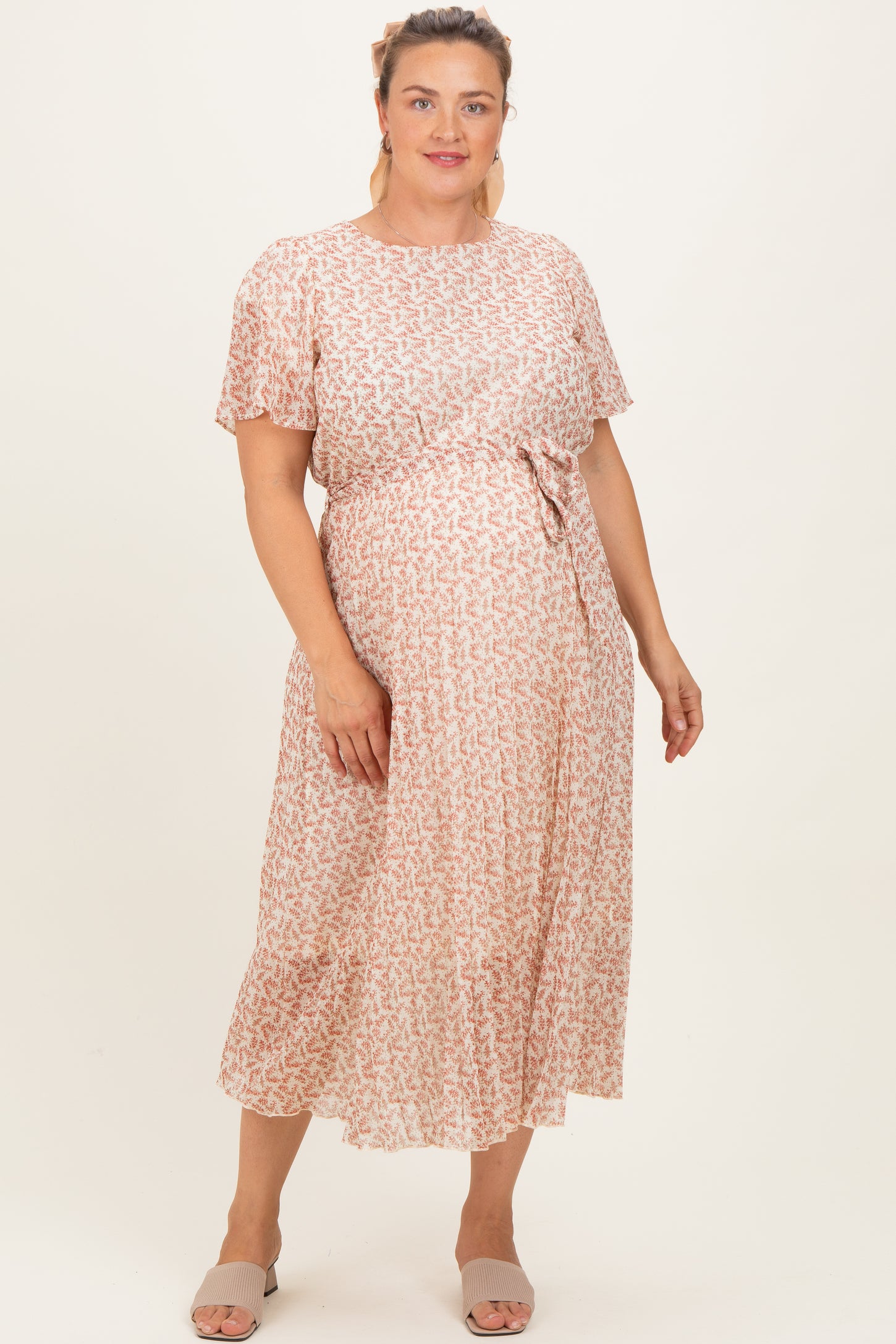 woman wearing a flowy pink and white patterned maternity dress with short sleeves and a tie waist, showing her baby bump